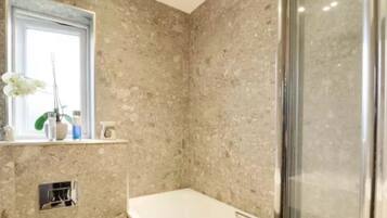 A bathroom with a marble wall, a window with an orchid, and a shower area.