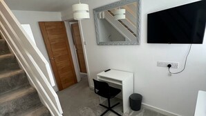 Une chambre moderne avec un escalier, un bureau blanc, un miroir, une télévision et une poubelle.