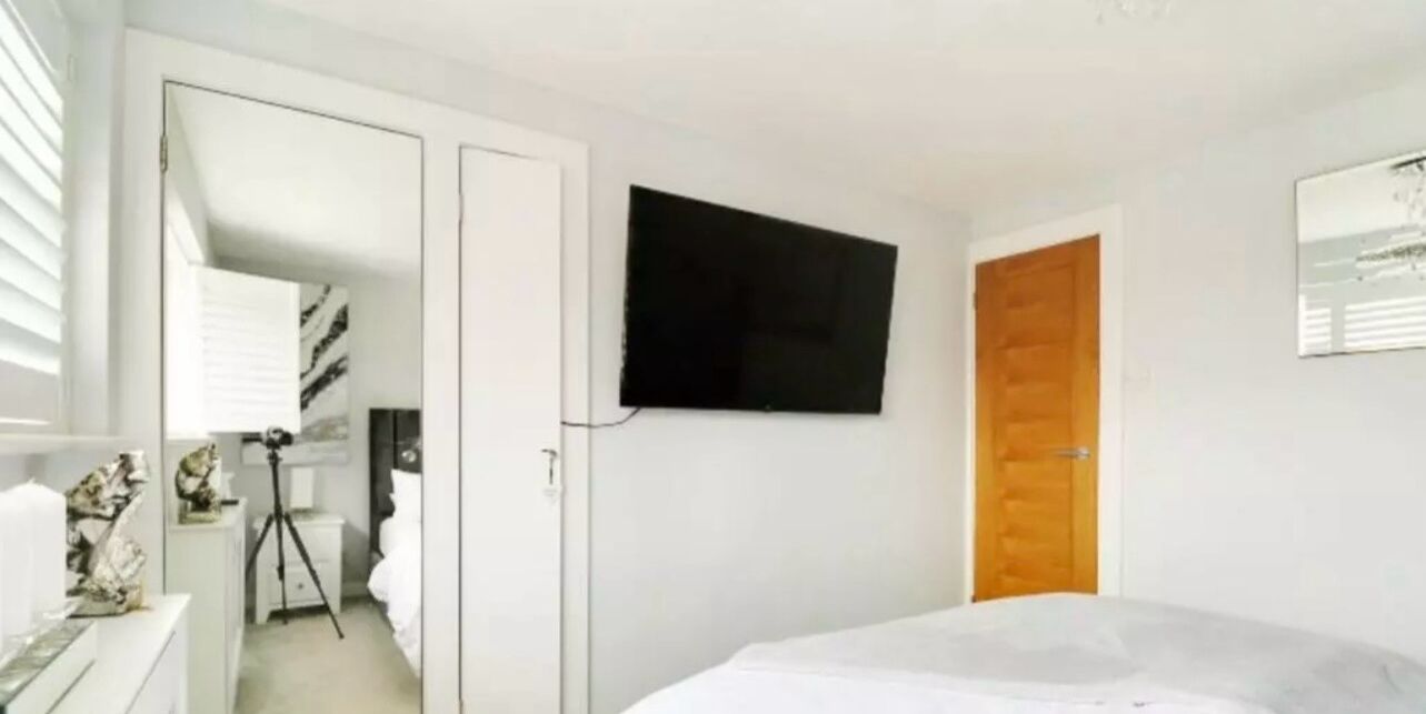 Une chambre à coucher avec un lit, un téléviseur fixé au mur, une porte en bois et une armoire blanche.