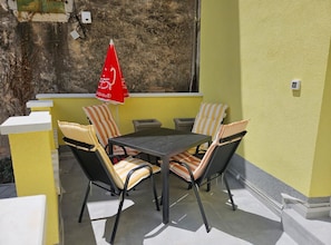 A patio with a table and four chairs, an umbrella, and a yellow wall.