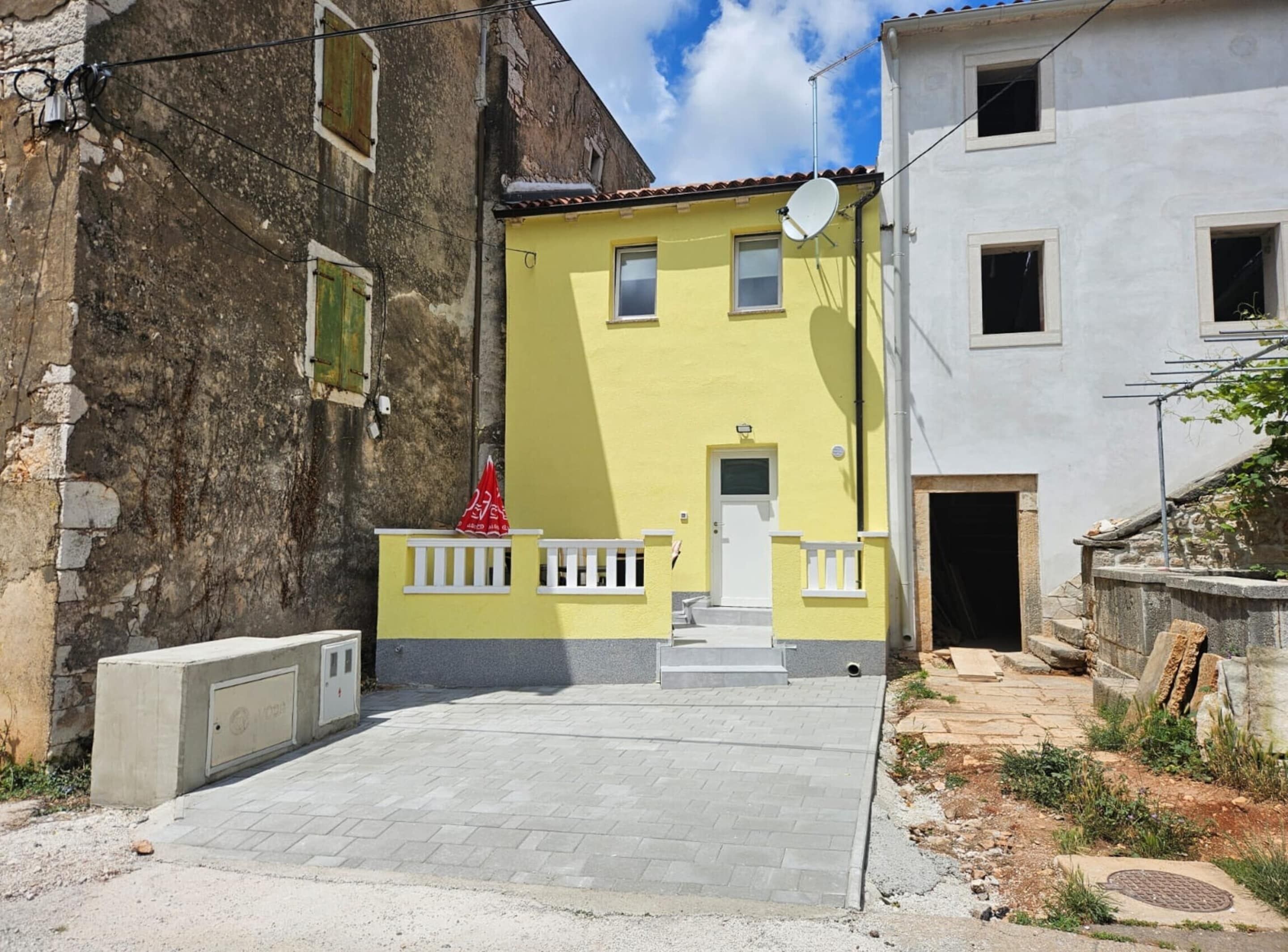 A narrow street with a yellow building featuring a white door and small windows.