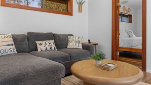 Una sala acogedora con un sofá gris, una mesa redonda de madera y cojines decorativos.