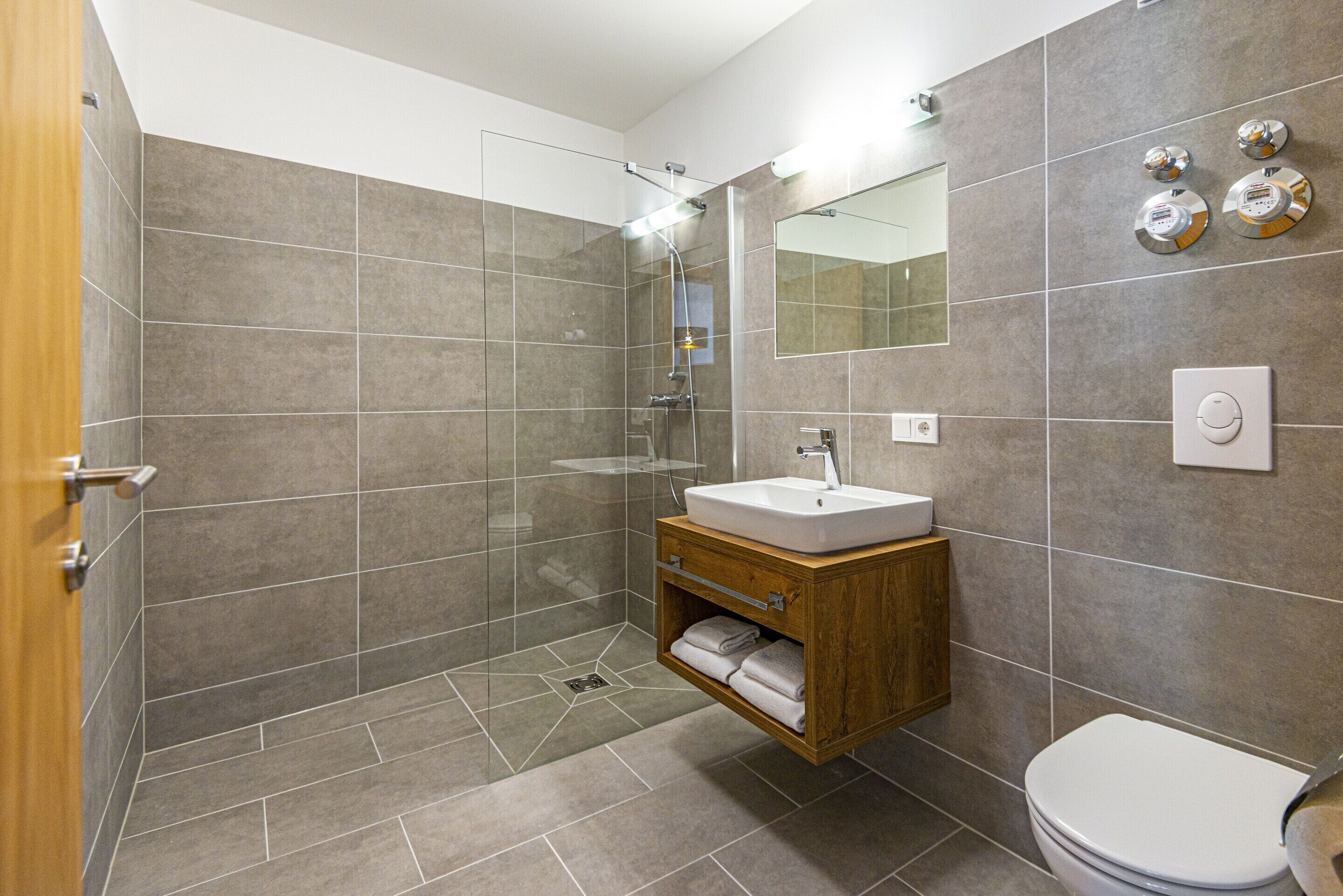 A modern bathroom with a glass-enclosed shower, a wooden vanity with a sink, and a toilet.