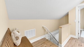 Una escalera con barandilla de madera, paredes color beige y techo blanco.