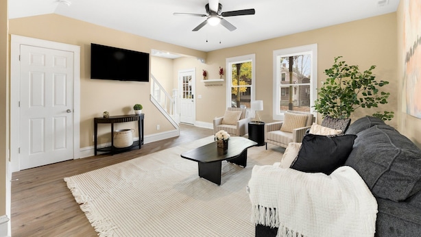 Una sala de estar con ventilador de techo, televisor, sofá, mesa de centro y una escalera que conduce a otra habitación.
