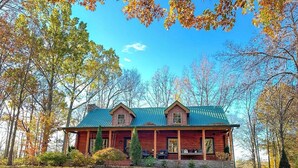 Een vakantiehuis in blokhutstijl met een groen dak, twee schoorstenen en een veranda met terrasmeubels.