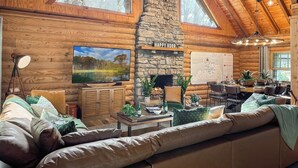 Een gezellig blokhutinterieur met een stenen openhaard, een grote flatscreen televisie en een eethoek.
