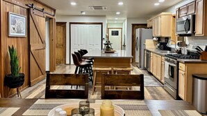 A modern kitchen with wooden cabinetry, a large island, and a dining area with wooden chairs. - Explore Oregon Outback - Sauna - Hot Tub - Stargaze - WIFI - Bird Watching (Summer Lake)