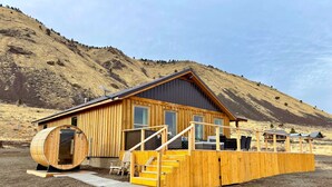 A wooden cabin with a large barrel-shaped sauna, a covered outdoor seating area, and a staircase leading to the entrance. - Explore Oregon Outback - Sauna - Hot Tub - Stargaze - WIFI - Bird Watching (Summer Lake)