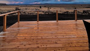 A wooden deck with a metal railing, overlooking a vast landscape with distant hills and a cloudy sky. - Explore Oregon Outback - Sauna - Hot Tub - Stargaze - WIFI - Bird Watching (Summer Lake)