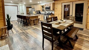 A spacious dining area with a wooden table and chairs, a kitchen in the background, and a ceiling fan. - Explore Oregon Outback - Sauna - Hot Tub - Stargaze - WIFI - Bird Watching (Summer Lake)
