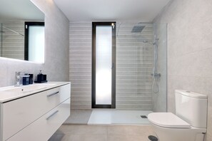 Ein modernes Badezimmer mit Duschkabine aus Glas, einer weißen Toilette und einem Waschtisch mit Spiegel und Stauraum.
