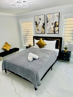 Relax in a serene bedroom with a large bed, minimalist decor, and a potted plant.