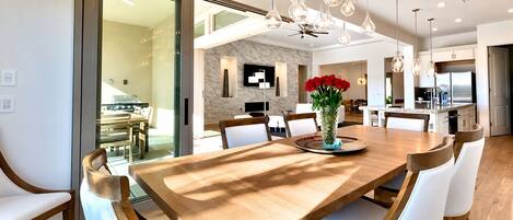 Un comedor moderno con una gran mesa de madera, sillas blancas tapizadas y un jarrón con flores rojas.