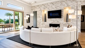 A modern living room with a curved white sofa, a flat-screen TV mounted on the wall, and a marble-patterned wall.