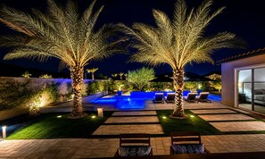 A modern outdoor pool area with lounge chairs and palm trees, surrounded by a well-lit patio.