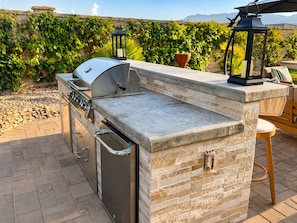 Una cucina esterna con barbecue integrato, lavello e piano di lavoro in pietra.