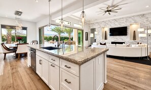 A modern kitchen with a large island, white cabinetry, and a view of the outdoors.