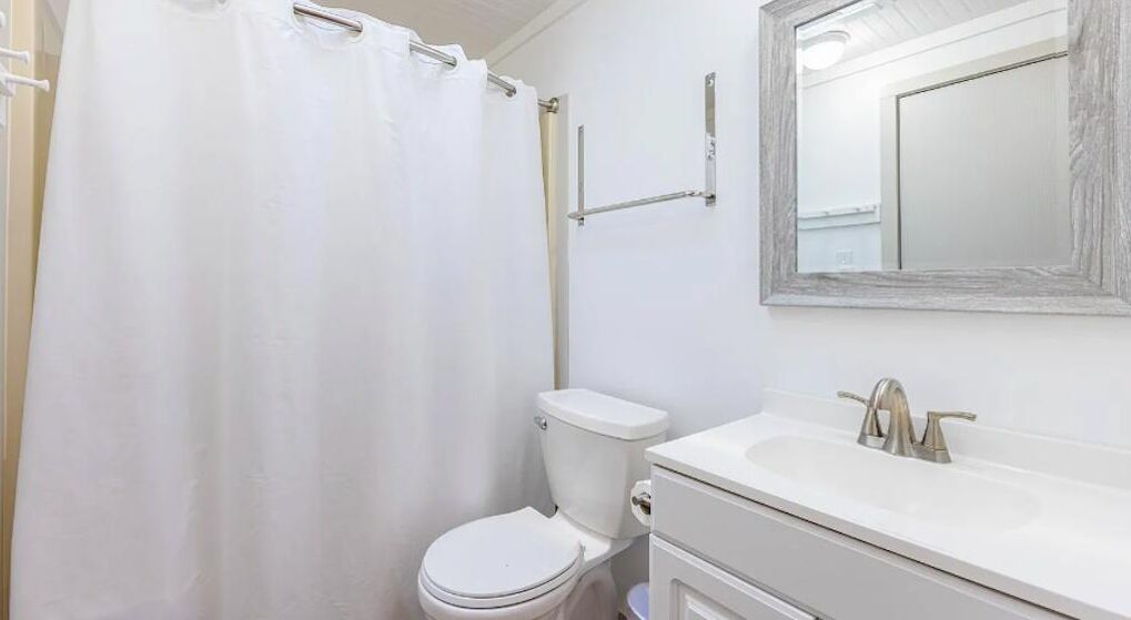 A bathroom with a white toilet, a sink with a mirror above it, and a shower curtain.