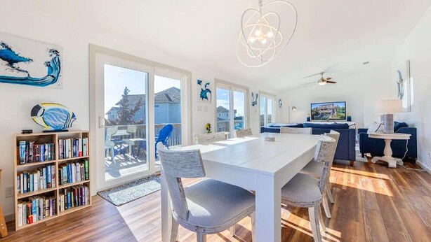 A spacious living area with a large white dining table, a bookshelf, and a blue sofa. - 4-bedroom house in welcoming Rodanthe with AC, WiFi. Enjoy your stay (Rodanthe)