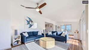 A modern living room with a blue sofa set, a round coffee table, and a ceiling fan. - 4-bedroom house in welcoming Rodanthe with AC, WiFi. Enjoy your stay (Rodanthe)