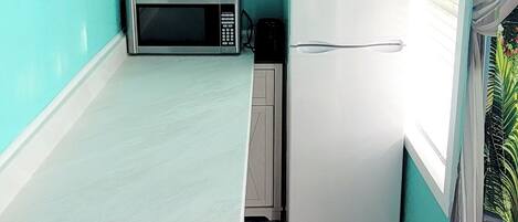 Una cocina pequeña con paredes color turquesa, una encimera blanca, un microondas y un refrigerador.