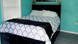 Una camera da letto con un letto, una finestra con persiane, un condizionatore fissato al muro e un quadro incorniciato sopra il letto.
