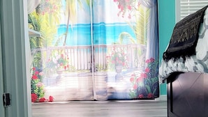 Una stanza con un'ampia porta-finestra scorrevole che dà su un balcone con un murale tropicale.
