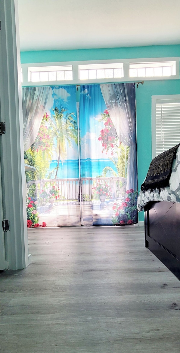 A room with a large sliding glass door leading to a balcony with a tropical mural. - Waterfront studio in amazing bay view with AC, WiFi (Baytown)