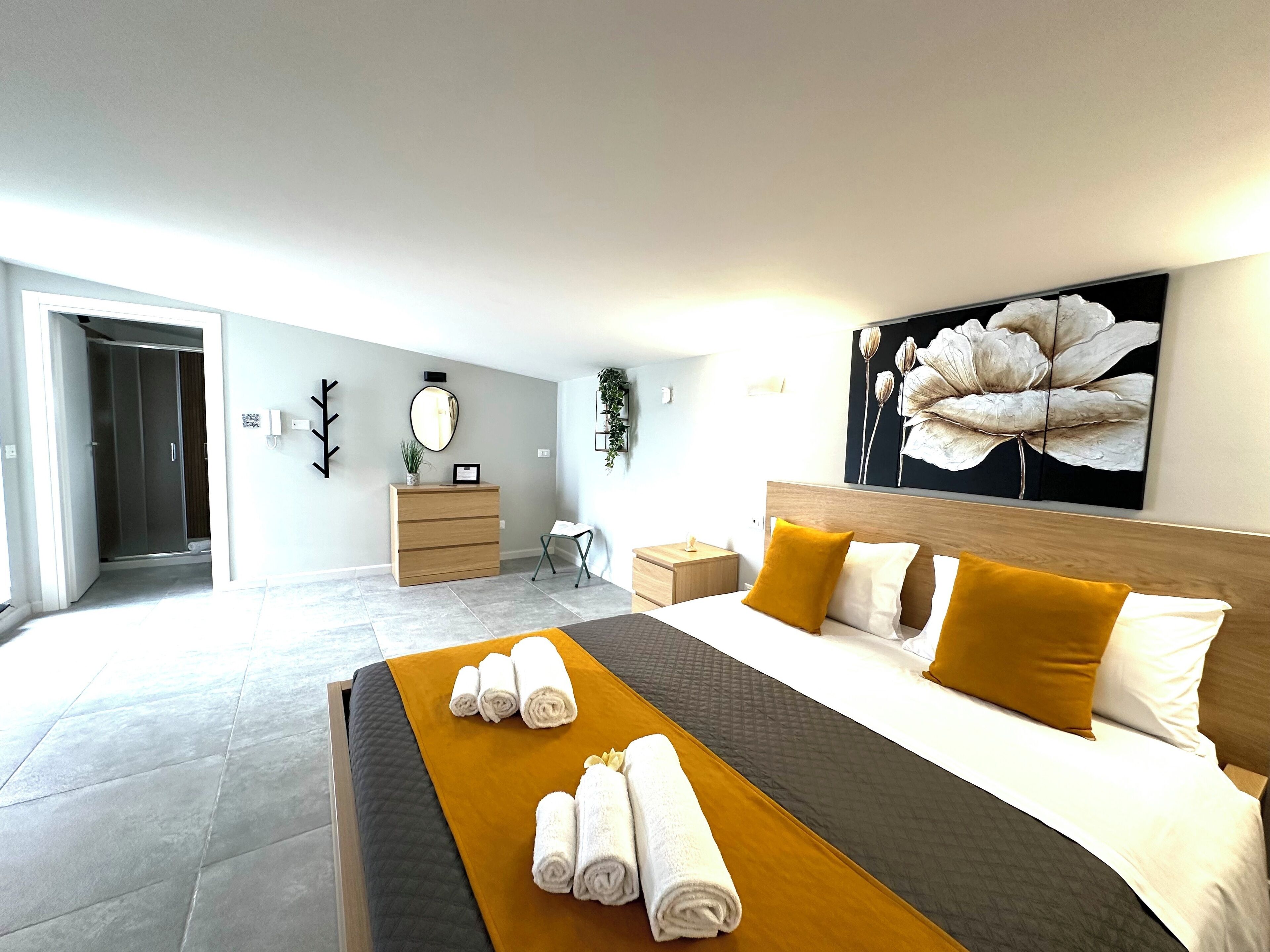 Une chambre d’hôtel moderne avec un grand lit, une commode en bois, un miroir et un tableau au mur.