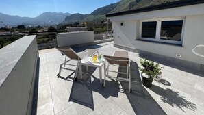 A rooftop terrace with a table and chairs, a potted plant, and a view of mountains. - Piante Del Principe Apartments and Rooms (Carini)
