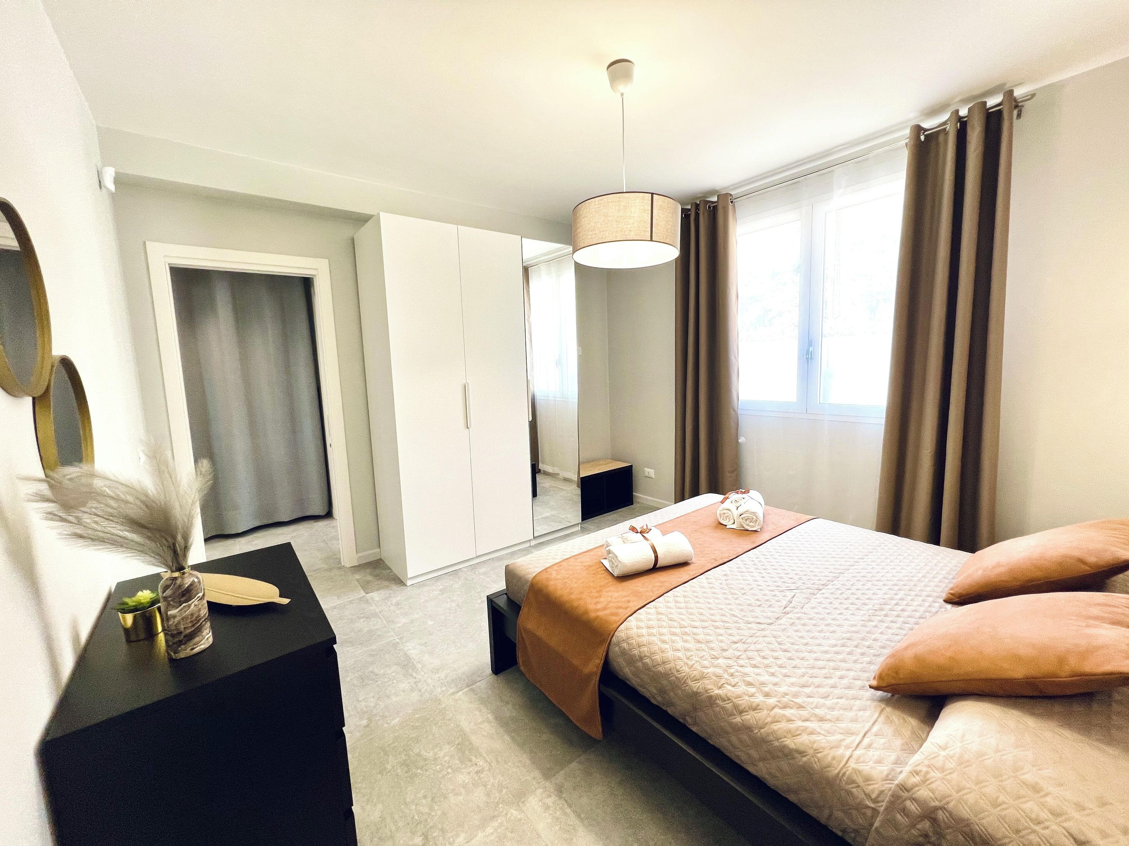 A modern hotel room with a bed, a desk, a wardrobe, and a large window with curtains.