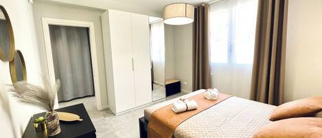 A modern hotel room with a bed, a desk, a wardrobe, and a large window with curtains.