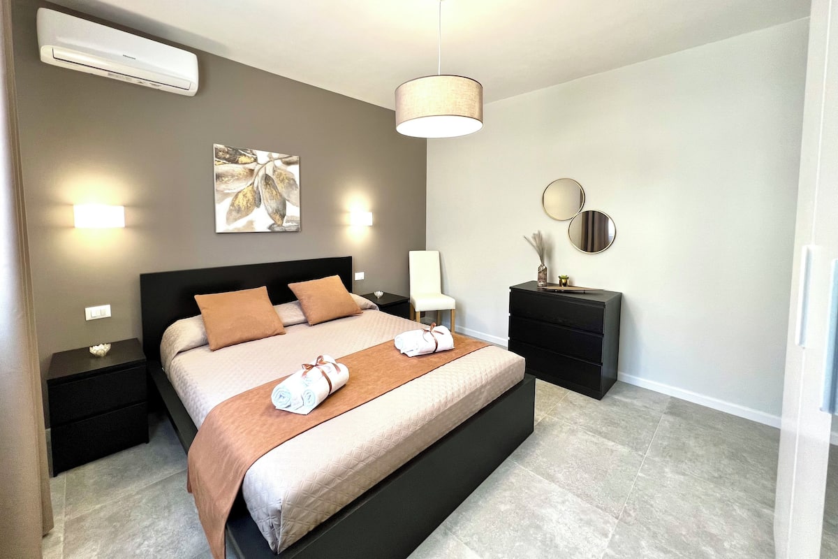 Un dormitorio moderno con una cama grande, mesitas de noche, una lámpara y espejos montados en la pared.