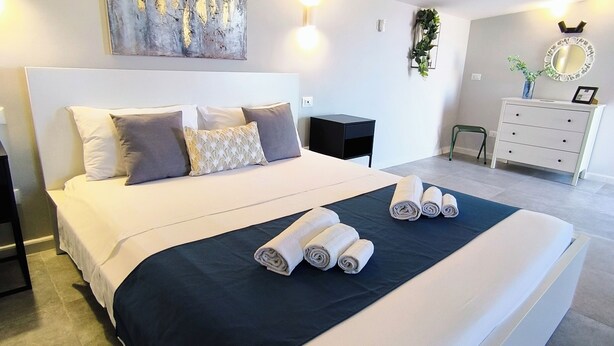 A modern bedroom with a large bed, a nightstand, a dresser, and a wall-mounted mirror. - Piante Del Principe Apartments and Rooms (Carini)