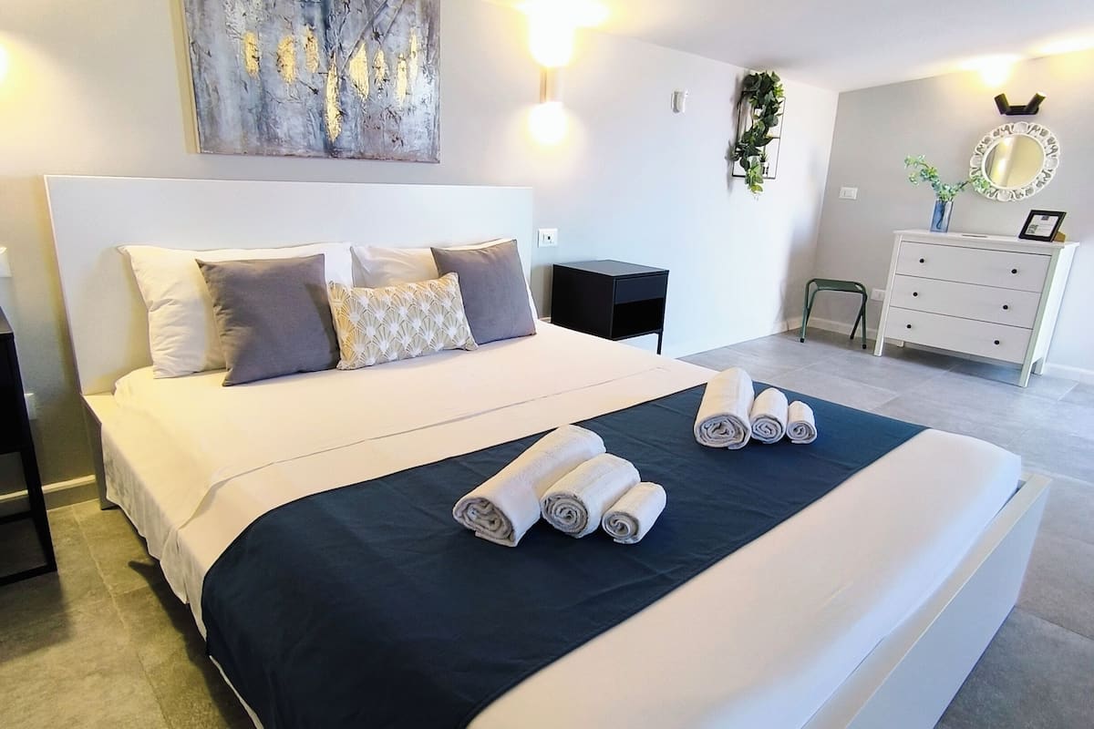 Un dormitorio moderno con una cama grande, una mesita de noche, un aparador y un espejo instalado en la pared.