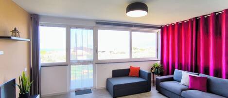 Un salon moderne avec un canapé gris, un fauteuil gris plus petit, un téléviseur à écran plat posé sur un meuble noir et une plante en pot.