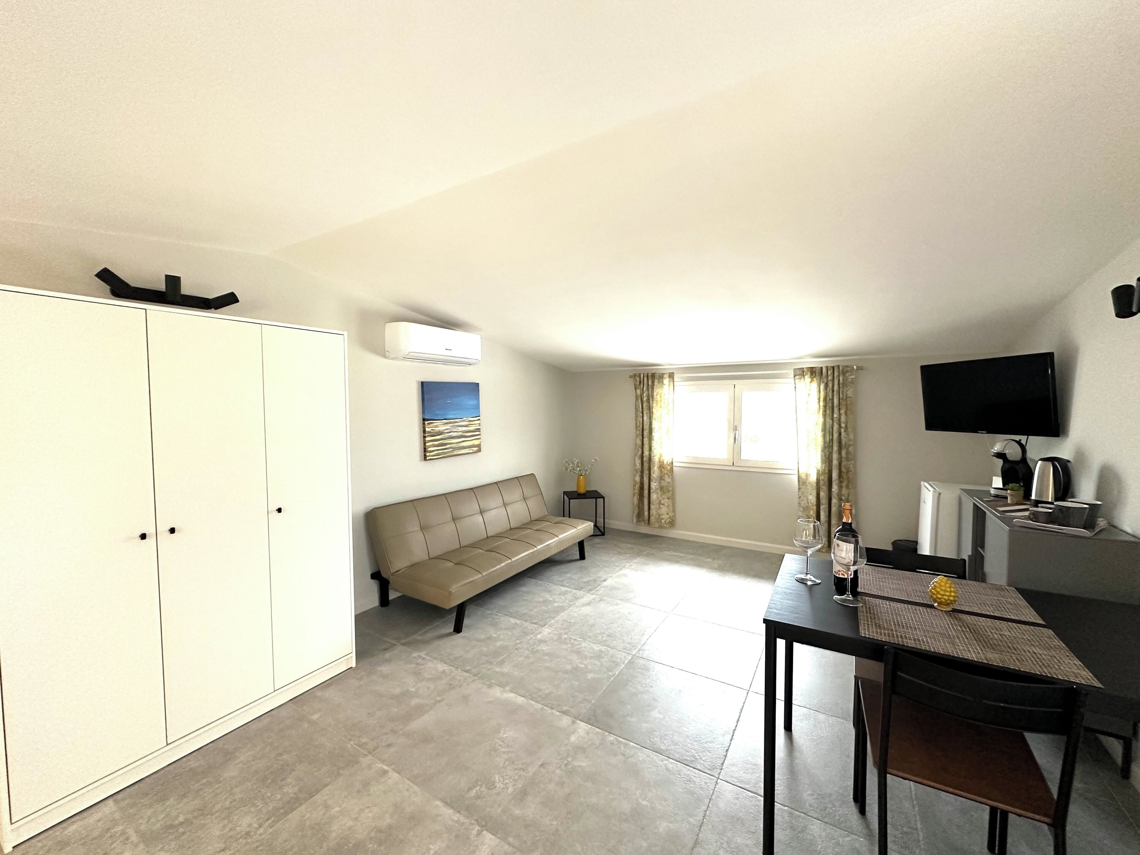 A spacious room with a sofa, a dining table with chairs, a TV, and a wardrobe.