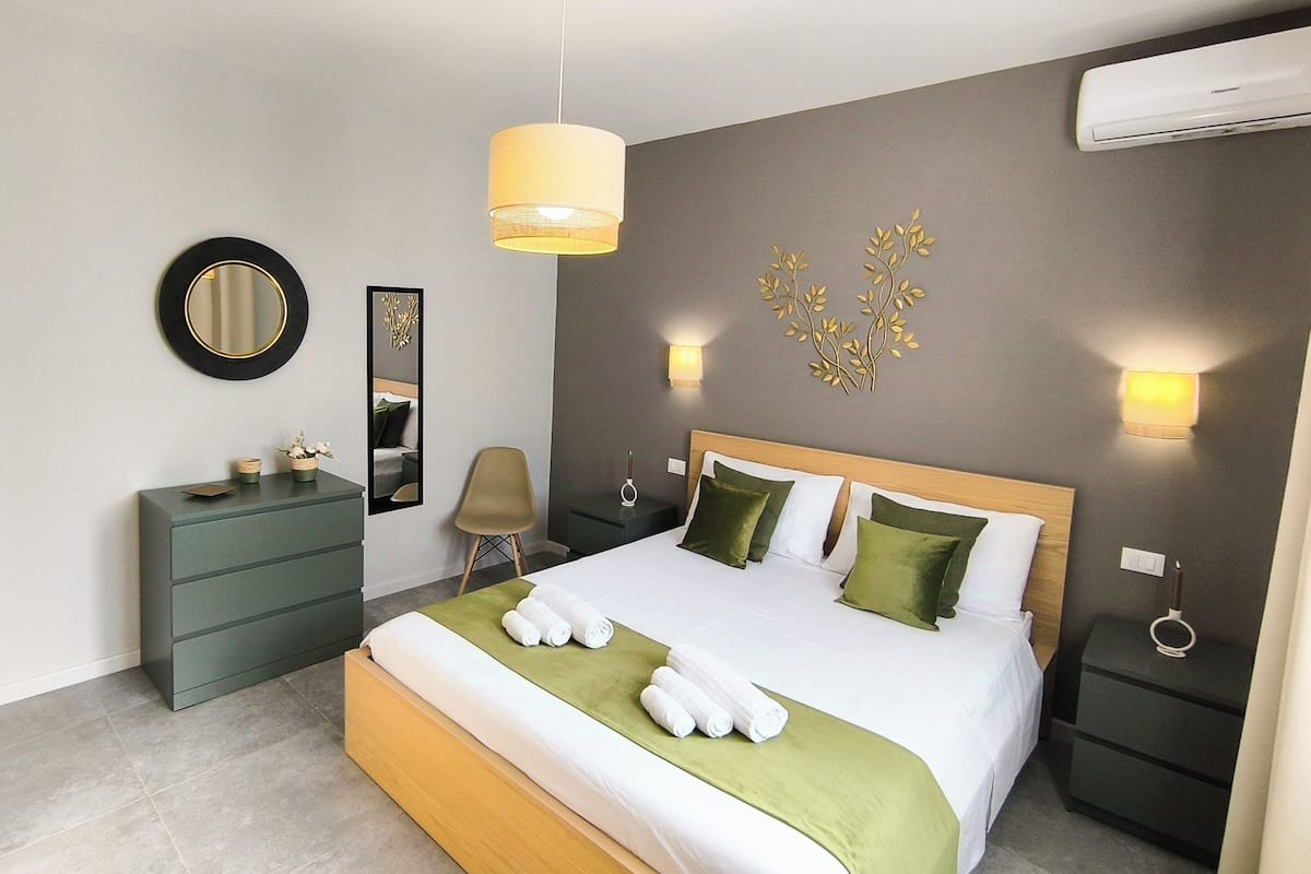 Una habitación de hotel moderna con una cama grande, mesitas de noche, un espejo e iluminación en la pared.