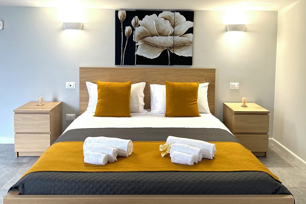 Un dormitorio moderno con una cama grande, dos mesitas de noche, una lámpara de pared y una obra de arte floral sobre la cama.