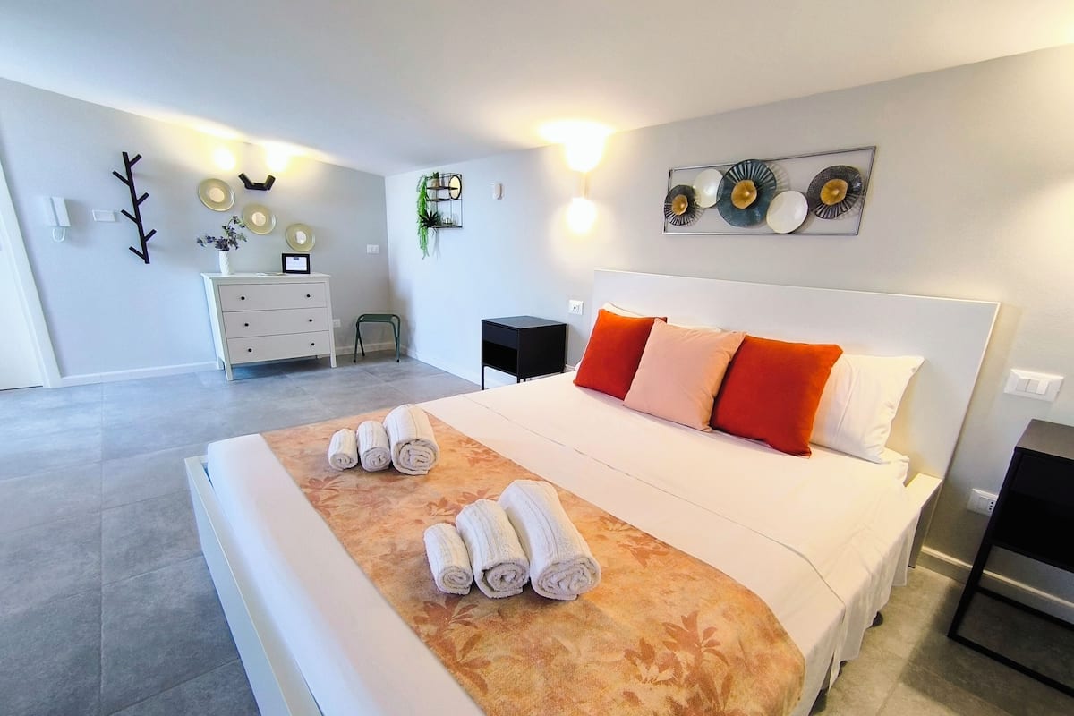 Una habitación de hotel moderna con una cama grande, una mesita de noche, un aparador y una lámpara de pared.