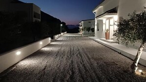 A nighttime view of a residential street with houses on either side, a gravel driveway, and street lighting. - Piante Del Principe Apartments and Rooms (Carini)