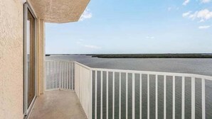 A balcony with a view of the sea, a white railing, and a beige wall.