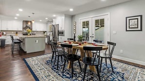 A modern kitchen with white cabinets, a central island, and a dining area with a wooden table and black chairs.
