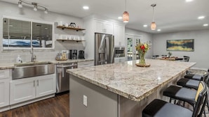 A modern kitchen with white cabinets, stainless steel appliances, a granite countertop, and pendant lighting.
