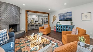 A living room with a fireplace, a blue sofa, an orange armchair, a coffee table, and a blue cabinet.