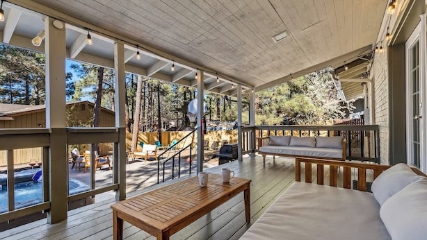 A covered outdoor area with a wooden deck, a sofa, a table, and a hot tub.
