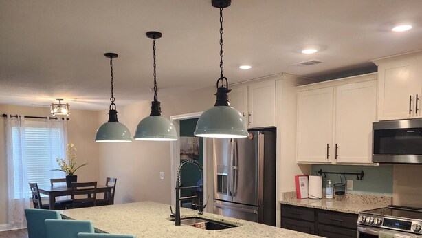 A kitchen with a central island, bar stools, stainless steel appliances, and pendant lighting.