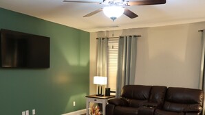 A living room with a brown leather sofa, a white coffee table, and a ceiling fan.
