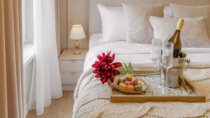 A hotel room with a neatly made bed, a bedside table with a lamp, a tray with snacks, and a bottle of champagne. - Parisian-Inspired 1BR in the Heart of Bucharest - Balcony, AC & Fully Equipped (Bucharest)